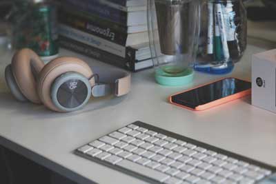 A desk with keyboard, headphones, teal cup, and an orange phone on it.
